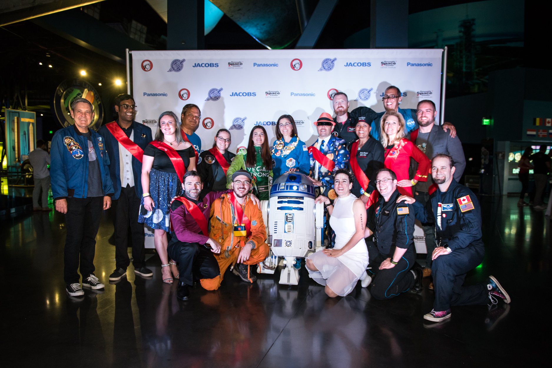 YN Space Coast 2018 Ambassadors stand and kneel in front of a sponsor banner